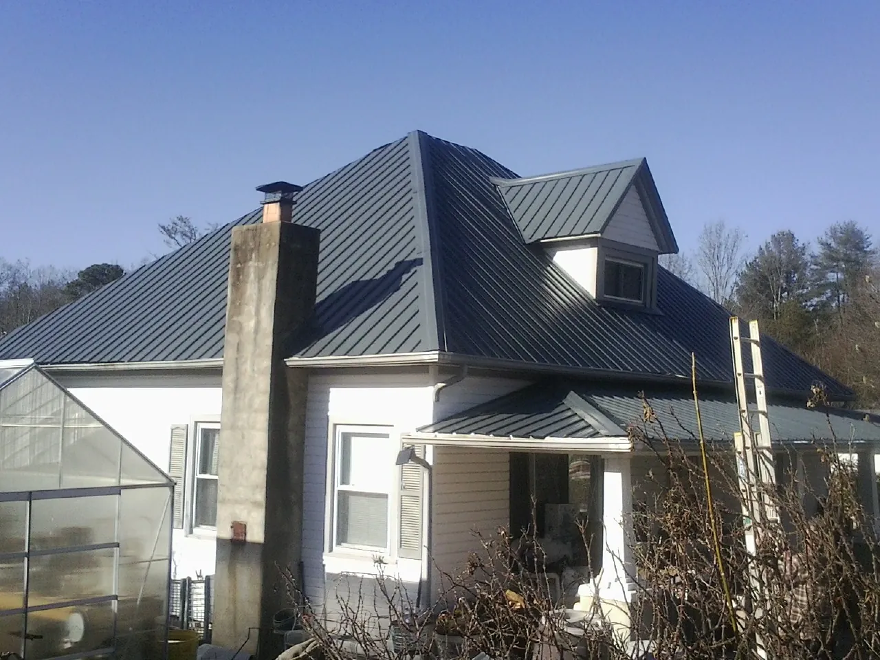 Dark blue standing seam metal roof on a white farmhouse with dormer — Slate & Tile Roof Repair by Roofing Brothers in Erieville