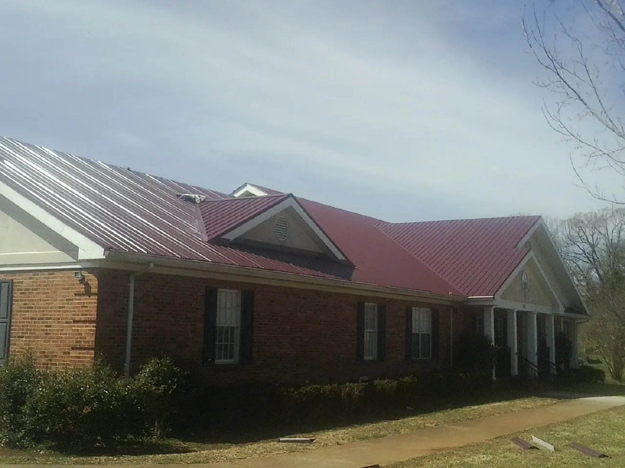 Red metal roof with gabled entries on a long brick building, from a Hail Damage Roof Repair job in Erieville