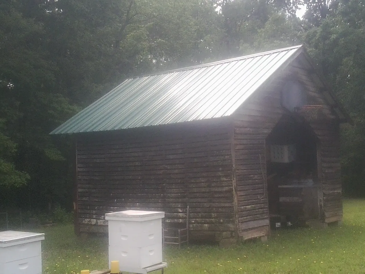 Green metal roof on a weathered barn beside stacked beehives in Erieville