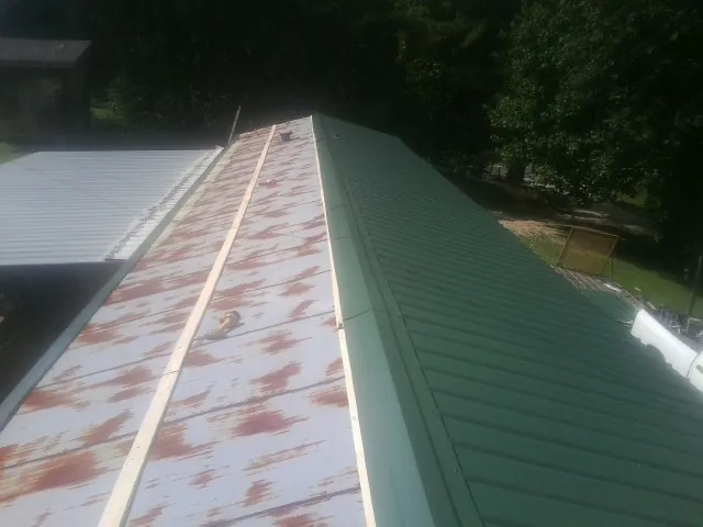 Old rusted panels beside newly installed green metal roofing — Wind Damage Roof Repair by Roofing Brothers in Erieville