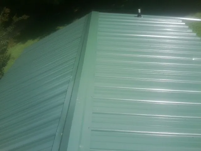 New green metal panels meeting at the ridge of a roof — Flat Roof Repair work by our crew in Erieville