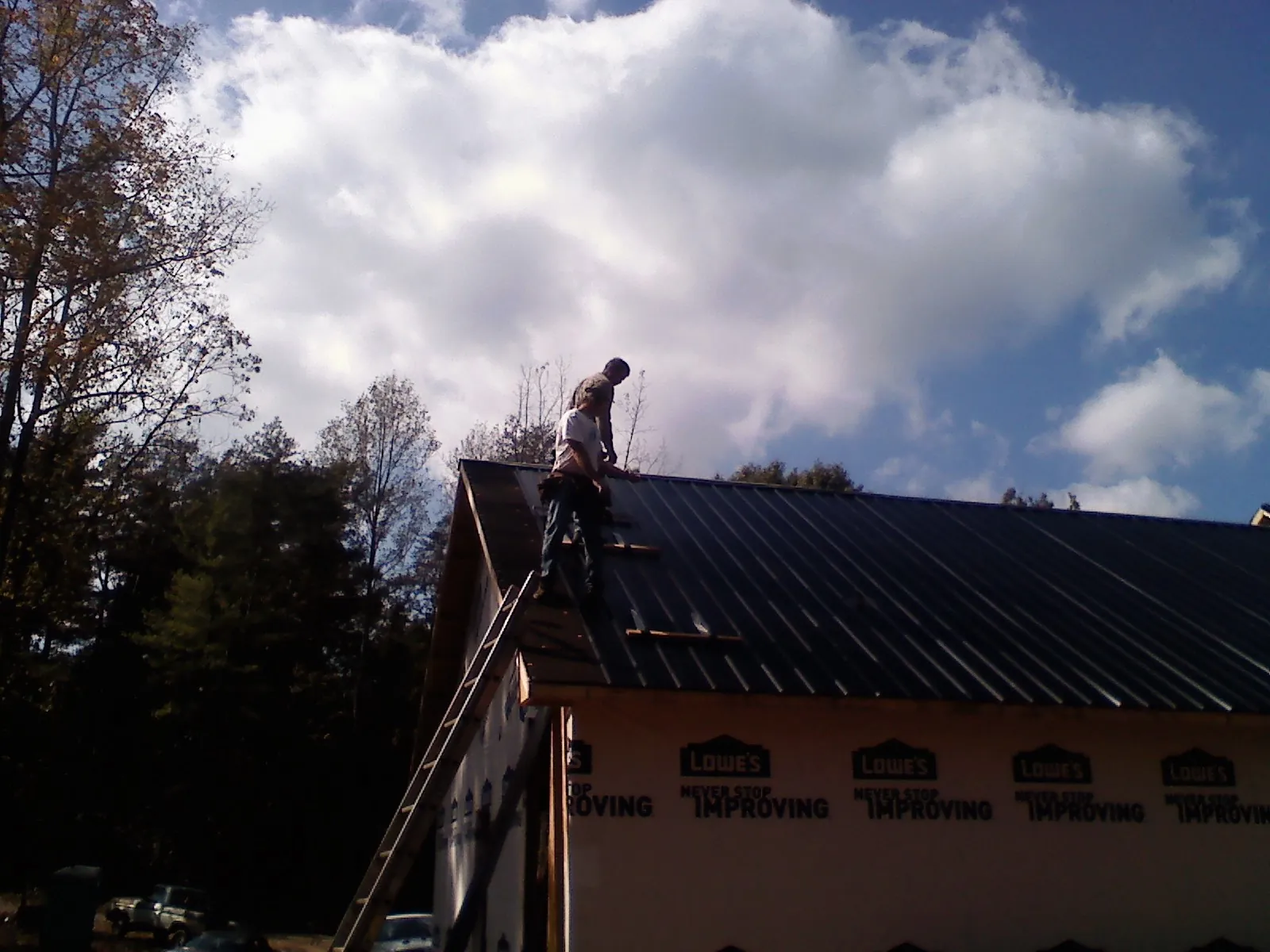 Roofer fastening dark metal panels high against a cloudy sky, from a Roof Inspection job in Erieville