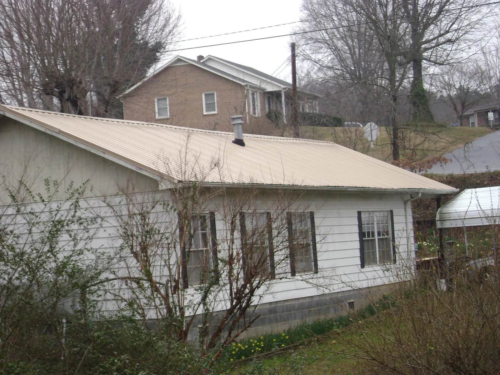 Tan metal roof on a white sided house set into a hillside — Commercial Roofing by Roofing Brothers in Erieville