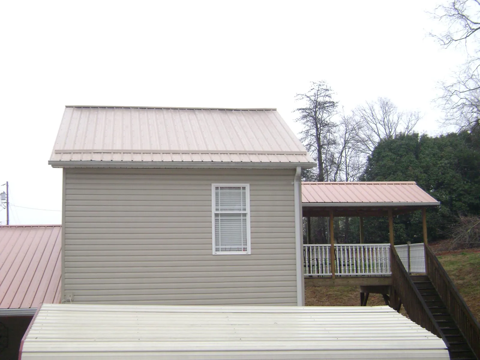 Tan metal roofs on a two story addition and attached porch, from a Roof Replacement job in Erieville